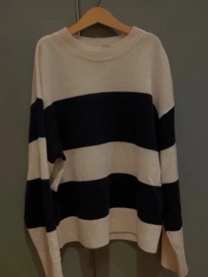 Randig stickad tröja i svart och beige - Stickad tröja med mörk blå och off white/beige ränder. Tröjan har rund halsringning, långa ärmar och ribbstickade muddar vid hals, ärmslut och nederkant. Den är XS och lite oversized. Jag har bara haft den på mig några gånger.
