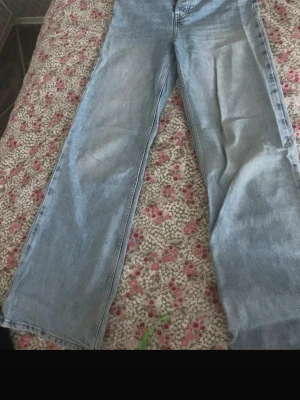 Ljusblå raka jeans i denim - Säljer ett par ljusblå jeans med rak passform och klassisk femficksdesign. Jeansen har en avslappnad look och är tillverkade i denim. Perfekta för dig som gillar en enkel och tidlös stil.