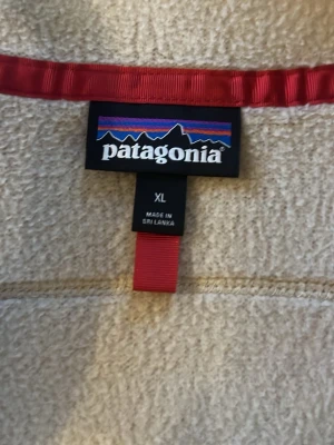 Beige fleeceväst från Patagonia XL - Snygg beige fleeceväst från Patagonia i storlek XL. Västen har svarta detaljer, röda dragkedjor och hög krage. Perfekt för lager-på-lager och outdoor-stil. Materialet är mjukt och värmande fleece, med tre fickor framtill.