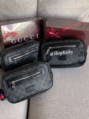 Svart magväska med monogram - Snygg svart handväska med klassiskt monogram i canvas och detaljer i läder. Väskan har en silverfärgad dragkedja framtill och ett stilrent, rektangulärt format. Perfekt för dig som gillar lyxiga accessoarer och vill sticka ut.