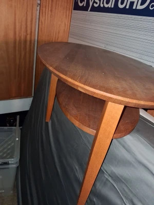 TANGO soffbord i mörkt trä - Säljer ett runt soffbord i mörkbrunt trä med en extra hylla undertill. Bordet har tre ben och en stilren, klassisk design som passar perfekt i vardagsrummet. Materialet är trä och formen är rund.