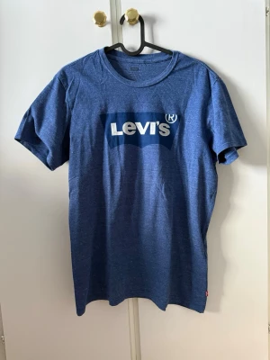 Levi's t-shirt  - Snygg blå t-shirt från Levi's med klassisk vit logga tryckt på bröstet. T-shirten har rund halsringning och korta ärmar. Perfekt till jeans eller shorts för en avslappnad look.