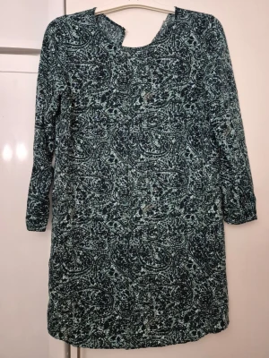 Klänning - Klänning med blågrönt abstrakt mönster och trekvartsärm. Klänningen har en avslappnad passform och en liten v-ringning vid halsen. Perfekt för dig som gillar unika prints och bekväma plagg.