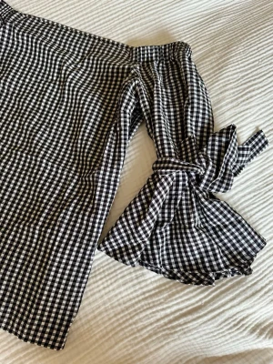 Offshoulder blus med svartvitt rutmönster - Svart-vit rutig blus. Längre trekvartsärmar med fina rosetter. Detta är verkligen en otroligt fin blus. 