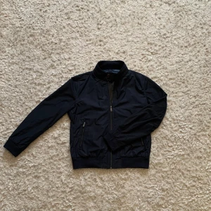 Marinblå vindjacka från Massimo Dutti - Säljer en sjukt snygg och stilren mörkblå vind/regn jacka från Massimo Dutti. Den är i mycket gott skick utan hål eller fläckar. Strl L men passar mig som brukar bära M.