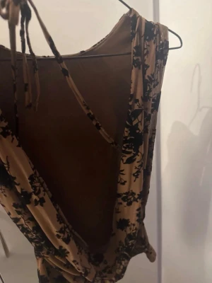 Brun rygglös topp - Säljer en brun topp med svart blommigt mönster och rygglös. mjukt, stretchigt material. 