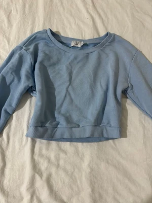 Ljusblå croppad sweatshirt NA-KD - Säljer en ljusblå croppad sweatshirt från NA-KD x Pamela. Tröjan har rund halsringning, långa ärmar och ribbade muddar vid ärmslut och nederkant. Perfekt för en avslappnad och trendig look. 🦋💙