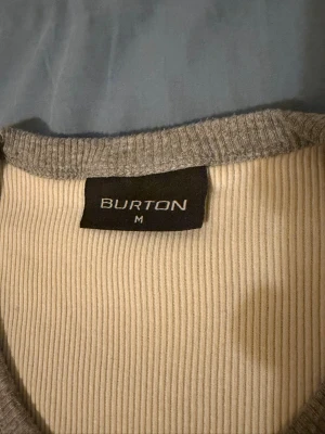 Grå ribbad t-shirt från Burton M - Säljer en stilren grå ribbad t-shirt från Burton i storlek M. T-shirten har v-ringning och korta ärmar, perfekt för en avslappnad look. Materialet känns mjukt och bekvämt, och den ribbade strukturen ger en snygg detalj.
