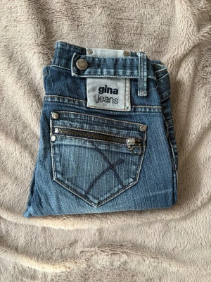 Vintage jeans - PRIS GÅR ATT DISKUTERA. Säljer ett par blå vintage jeans från Gina Jeans med cool dragkedjedetalj på bakfickan och dekorativ söm. Klassisk femficksmodell i tvättad denim med raka ben och bälteshällor. Perfekta för en avslappnad och trendig look. Dom är raka/skinny, men skulle nog vara supersnygga att göra om till bootcut eller sy om till en kjol nu till sommarn😍Köpta mellan 1985-2005 så därav går dom inte längre att få tag på💗
