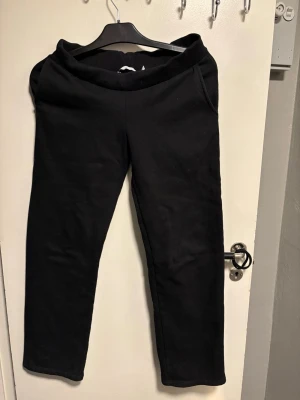 Svarta mjukisbyxor med resårmidja - Ett par klassiska svarta mjukisbyxor med bred resår i midjan och raka ben. Tillverkade i mjukt och bekvämt material, perfekta för chill dagar hemma eller när du vill ha det extra bekvämt. Inga synliga loggor eller detaljer.