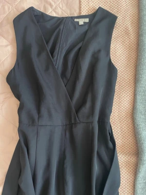 Svart ärmlös byxdress från H&M - Stilren svart byxdress från H&M med omlott-ringning och ärmlös design. Den har ”old money” viben. Jag har aldrig funnit mig själv i en situation då jag haft på mig den här, men materialet är otroligt mjukt och byxdressen är i gott skick utan defekter.