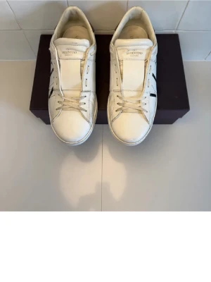 Valentino skor - Snygga vita sneakers från Valentino med svarta grafiska detaljer på sidorna och svart hälparti. Skorna har klassisk låg modell, rund tå och vita snören. Tillverkade i läder med diskret logga på plösen. Perfekta för dig som gillar stilrena men ändå unika sneakers.  (Äkta)