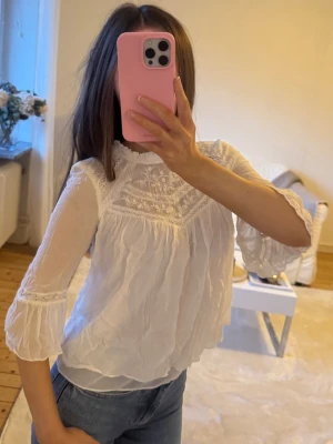 Vit boho blus med spetsdetaljer - Superfin vit blus med broderade spetsdetaljer och lätt transparent tyg. Blusen har trekvartsärm med volang och hög halsringning. 