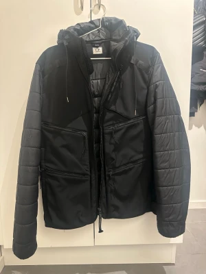 C.P Company Jacka - Säljer en svart Goggle Jacket från C.P. Company med ikoniska glasögon i huvan.   Jackan har quiltade ärmar, flera dragkedjefickor och justerbar huva. Finns flera skavanker som jag bifogat på bilden. Men allmänt i fint skick.  Köpt på SEASON på Asecs för några år sen av min pojkvän, han har inget kvitto kvar men man kan skanna den via en QR-kod för att se att den är äkta. Storlek 50 vilket ska motsvara medium.   Köpt för 5500kr, mitt pris är 1000kr