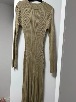 Beige ribbad långklänning - Snygg beige långklänning med ribbad struktur och lång ärm. Klänningen har en kroppsnära passform och rund halsringning. Perfekt för dig som gillar stilrena och enkla plagg med en twist.