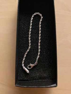 Ropechain stilrent armband 5mm - Ett stilrent armband i silverfärg med tvinnad kedja och karbinhake. Perfekt accessoar för att lyfta din outfit med en enkel men elegant touch. Materialet är metall och designen är klassisk och tidlös.