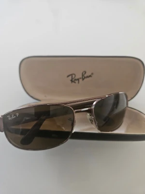 Bruna Ray-Ban solglasögon metallbåge - Snygga solglasögon från Ray-Ban med bruna glas och smal metallbåge. Klassisk design med Ray-Ban-logga på linsen. Kommer med originalfodral. Perfekta för soliga dagar och ger en cool look.