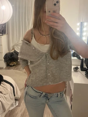 Grå cropped kofta med pärlknappar - Säljer en grå, cropped kofta med pärlknappar framtill. Koftan har en mjuk och tunn stickning, långa ärmar och en avslappnad passform. Perfekt att styla över ett linne eller t-shirt för en chill look. nopprig men fint skick 
