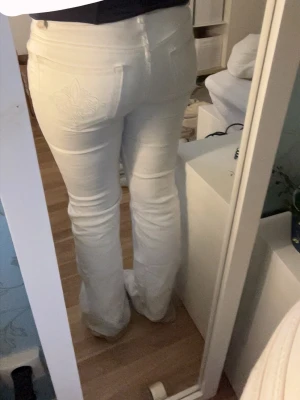 Vita bootcut jeans med broderad ficka - Säljer ett par vita bootcut jeans med snygg broderad detalj på bakfickan från lager 157. Jeansen har låg midja och är i fint skick. Perfekta för dig som vill ha en clean och fräsch look.