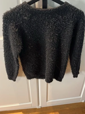 Svart fluffig stickad tröja från New Look - Mysig svart stickad tröja från New Look med fluffig textur. Tröjan har rund halsringning och långa ärmar, perfekt för kalla dagar. Enkel och stilren design som passar till många outfits.