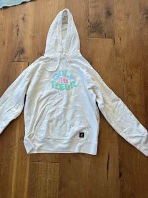 Vit Golf le Fleur hoodie Converse - Vit hoodie från Converse x Golf le Fleur med färgglad logga på bröstet. Klassisk känguruficka framtill och justerbar huva. Mjuk bomullskänsla och avslappnad passform, perfekt för en chill streetwear-look.