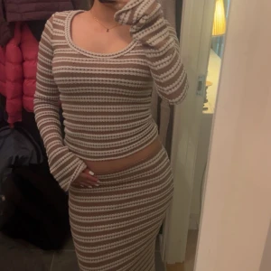 Randig långklänning i beige och vit - Säljer en långärmad set med beige och vita horisontella ränder. Settet har en rundad urringning och är figurnära med stretchigt material. Perfekt för dig som gillar en stilren och trendig look med lite boho-vibe.