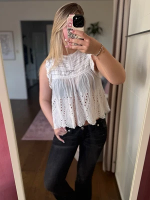 Vit broderad blus med volang - Söt vit blus med broderade detaljer och volangkant. Ärmlös modell med rund hals och luftig passform, perfekt för varma dagar. Blusen har ett romantiskt uttryck med fina hålbroderier och lätt struktur i tyget💗 Liten defekt (bild 3)