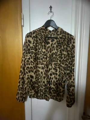 Leopardmönstrad tröja  - Snygg tröja med leopardmönster i bruna och svarta toner. tröjan har långa ärmar, knäppning framtill och en avslappnad passform. Perfekt för dig som vill sticka ut med ett djuriskt print.