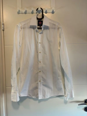 Vit skjorta  - Klassisk vit skjorta med lång ärm och knappar framtill. Skjortan har en stilren design med normal passform och är tillverkad i mjuk bomull. Perfekt till både jeans och chinos för en clean look.