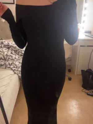 Svart offshoulder långklänning - Svart långklänning med offshoulder design och långa ärmar. Klänningen har en tight passform och framhäver ens figur så bra. Materialet är silkesliknande. Aldrig använd