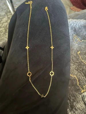 Guldigt halsband med cirklar och blommor - Snyggt halsband i guldfärgad metall med tunna länkar och dekorativa detaljer i form av små cirklar och blommor längs kedjan. Perfekt för att ge din outfit en elegant touch. Justerbar längd med klassiskt lås.