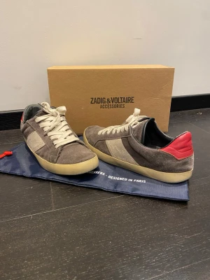 Zadig & Voltaire sneakers - Snygga sneakers från Zadig & Voltaire i grå mocka med beige detaljer och vit sula. Kommer med originalkartong och dustbag. Oanvända sulor. 
