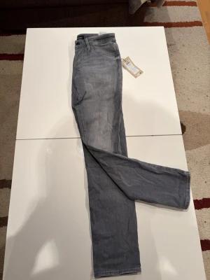 Ljusgrå raka jeans från Jack N Jones - Snygga ljusgrå jeans från Jack N Jonesmed rak passform och klassisk femficksdesign. Jeansen har bälteshällor, knappgylf och är tillverkade i mjukt denimtyg. Perfekta för en avslappnad och trendig stil. Storlek 28/32 modell: slim Glenn, grey Denim