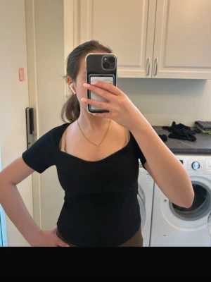 Svart croppad topp med unik halsringning - Säljer en svart croppad topp med cool, asymmetrisk halsringning och korta ärmar. Toppen har en tight passform och är perfekt för dig som gillar stilrena plagg med en twist. Materialet känns mjukt och stretchigt, vilket gör den bekväm att bära.