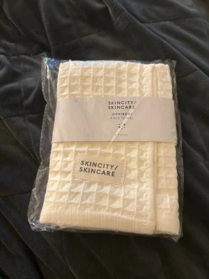 Vita ansiktshanddukar Skincity Skincare - Säljer ett set vita ansiktshanddukar från Skincity Skincare. Handdukarna har en snygg rutstruktur och är tillverkade i mjukt tyg, perfekta för hudvårdsrutinen. Kommer i originalförpackning och är märkta med Skincity Skincare-loggan.