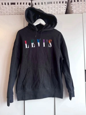Svart hoodie från Levi's med färgglad logga. S - Snygg hoodie från Levi's. Den är inte kolsvart utan mörkt gråsvart. Storlek S. Använd, ev lite blekare vid sömmar, och lite ytludd på muddar. Men är i fint skick. 
