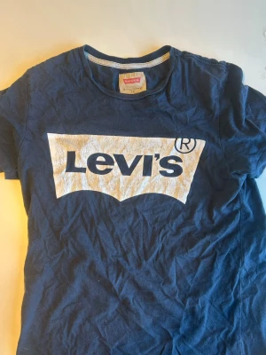 Blå Levi's t-shirt med stor logga - Snygg marinblå t-shirt från Levi's med stor vit logga framtill. Klassisk rund halsringning och korta ärmar. Tillverkad i mjuk bomull som känns skön mot huden. Perfekt för dig som gillar streetwear och vill ha en ikonisk look.