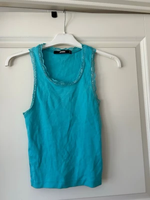 Turkos topp med spets från BikBok - Snygg turkos topp från BikBok i storlek XS. Toppen har spetsdetaljer runt halsringningen och ärmarna, vilket ger en söt touch. Perfekt till sommaren och enkel att matcha med jeans eller kjol. Jag har själv använt den bara en gång!