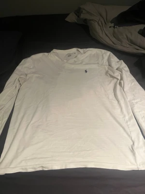 Vit långärmad från Ralph Lauren - Klassisk vit långärmad topp från Ralph Lauren med rund halsringning och den ikoniska broderade loggan på bröstet. Tillverkad i mjuk bomull som känns skön mot huden. Perfekt basplagg för en clean och stilren look.