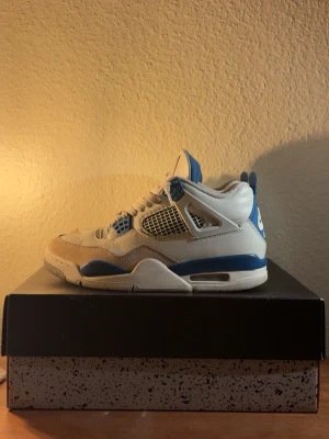 Nike Air Jordan 4 Retro  - Säljer ett par Nike Air Jordan 4 Retro sneakers i vitt och blått. Skorna har klassisk snörning, meshdetaljer på sidorna och ikonisk Nike Air-logga på hälen. Tillverkade i skinn och syntetmaterial med blåa och vita kontraster. Skorna är 100% äkta. Pris kan diskuteras!