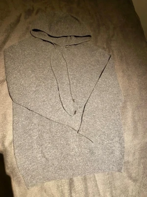 Grå stickad hoodie  - Mysig grå hoodie i mjukt stickat material med huva och dragsko. Klassisk modell utan tryck eller logga, perfekt för en chill och avslappnad stil. Passar lika bra till jeans som till mjukisbyxor.