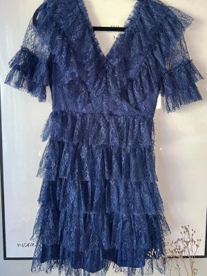 Blå spetsklänning med volanger - Supersöt blå BYMALINA klänning i spets med flera lager volanger och v-ringning. Klänningen har korta ärmar och är tillverkad i ett tunt spetsmaterial som ger en elegant känsla. Perfekt för dig som vill sticka ut med en feminin look. Använd 3 gånger, nypris 2800. Pris kan diskuteras.