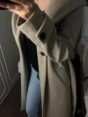 Beige kappa med luva,band och fickor  - En tjockare kappa från ZARA som håller värmen när det blir kallare. Jättefin och perfekt längd når knäna + har luva.