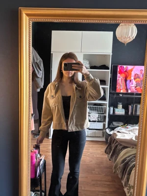 Beige kort jacka  - Säljer en beige jacka med stora bröstfickor och knappar framtill. Jackan har en avslappnad passform, klassisk krage och långa ärmar med breda muddar. Perfekt nu till våren och sommaren.