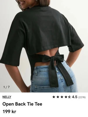 Nelly Svart tie top, öppen rygg och knyt - Trendig svart t-shirt från Nelly med öppen rygg och stor knytning bak. Modellen är croppad och har korta ärmar. Perfekt för dig som vill ha en unik och snygg detalj på din outfit. Tillverkad i mjuk bomull för skön känsla.