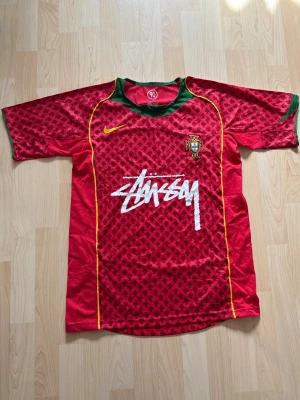 Portugal x Stüssy 2004 Special Edition - Stilren fotbollströja i helt nytt skick. Tröjan är inte använd en endaste sekund. Portugal tröjan kombineras med det exklusiva streetwear märket Stüssy.