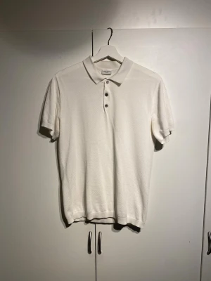 Vit pikétröja från John Henric - Klassisk vit pikétröja från John Henric med krage och tre knappar framtill. Tillverkad i ett mjukt material med korta ärmar och stilren design. Perfekt till jeans eller shorts för en clean look. storlek M och true to size. 