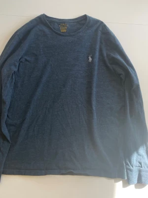 Mörkblå långärmad tröja Polo Ralph Lauren - Mörkblå långärmad tröja från Polo Ralph Lauren med rund halsringning och den klassiska broderade logotypen i vitt på bröstet. Tröjan har en enkel och stilren design, perfekt för en avslappnad look.