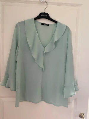 Ljusgrön volangblus från Mango - Ljusgrön blus från Mango med v-ringning och bred volangkant längs halsen. Blusen har långa, lätt utsvängda ärmar och är gjord i ett tunt, flowy material som ger en luftig känsla. Perfekt för dig som gillar en feminin och trendig stil. Kolla gärna mina andra annonser❗️