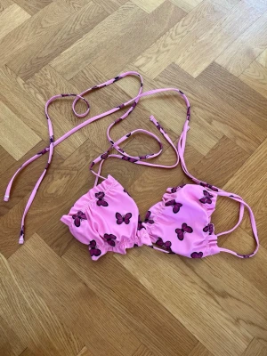 Rosa bikiniöverdel med fjärilar - Supersöt rosa bikiniöverdel från Shein med lila och mörkrosa fjärilar. Modellen har smala axelband och knyt i ryggen för justerbar passform. Materialet är mjukt och stretchigt, perfekt för lata dagar på stranden.